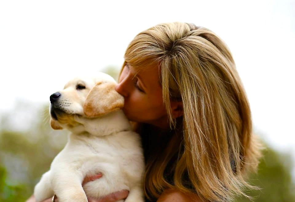 A woman hugs and kisses a soft yellow puppy during a moment outdoors.