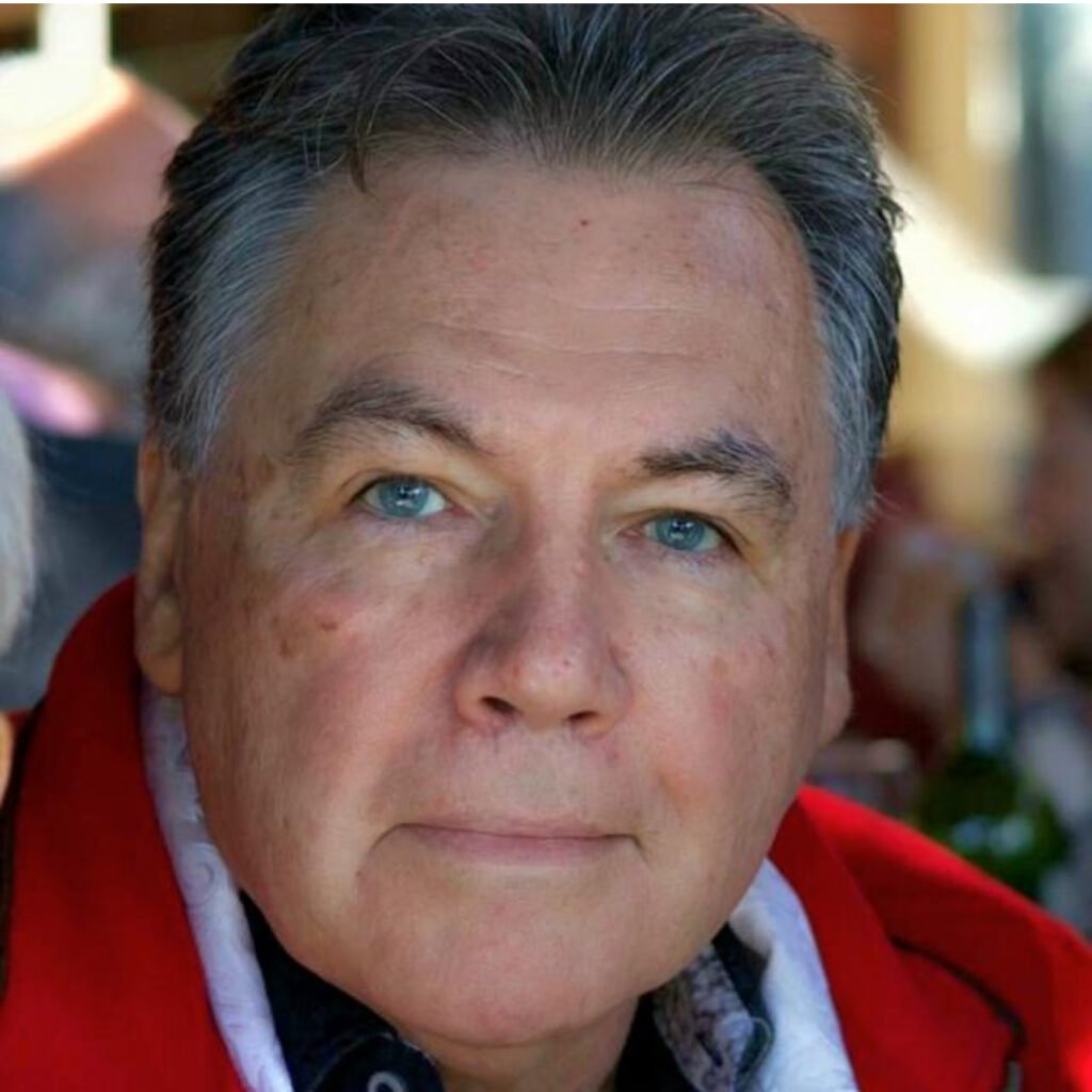 An older man wearing a red jacket with blue eyes in natural light.