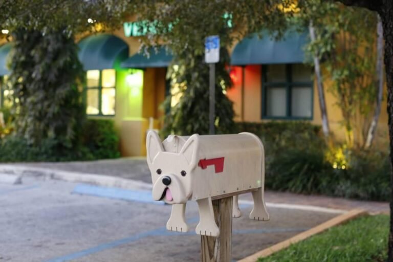 Dog-shaped mailbox standing in front of a veterinary clinic building with green awnings and soft evening lighting.